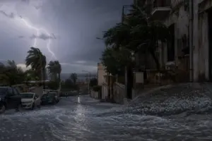 Strada in discesa durante un temporale con fulmini, grandine e acqua che scorre, palme piegate dal vento