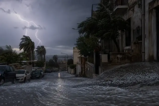 Strada in discesa durante un temporale con fulmini, grandine e acqua che scorre, palme piegate dal vento