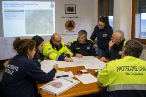 Volontari della Protezione Civile e assistenti sociali riuniti intorno a una mappa per pianificare l’emergenza