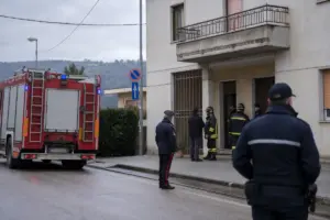 Camion dei vigili del fuoco e carabinieri davanti all’ingresso di un palazzo residenziale in una giornata nuvolosa