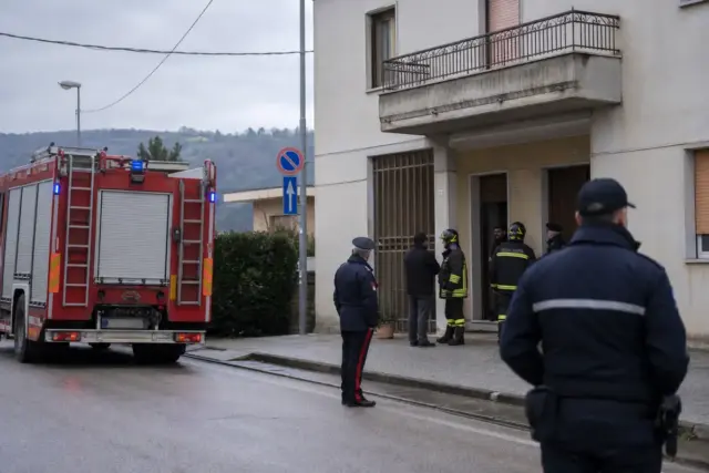 Camion dei vigili del fuoco e carabinieri davanti all’ingresso di un palazzo residenziale in una giornata nuvolosa