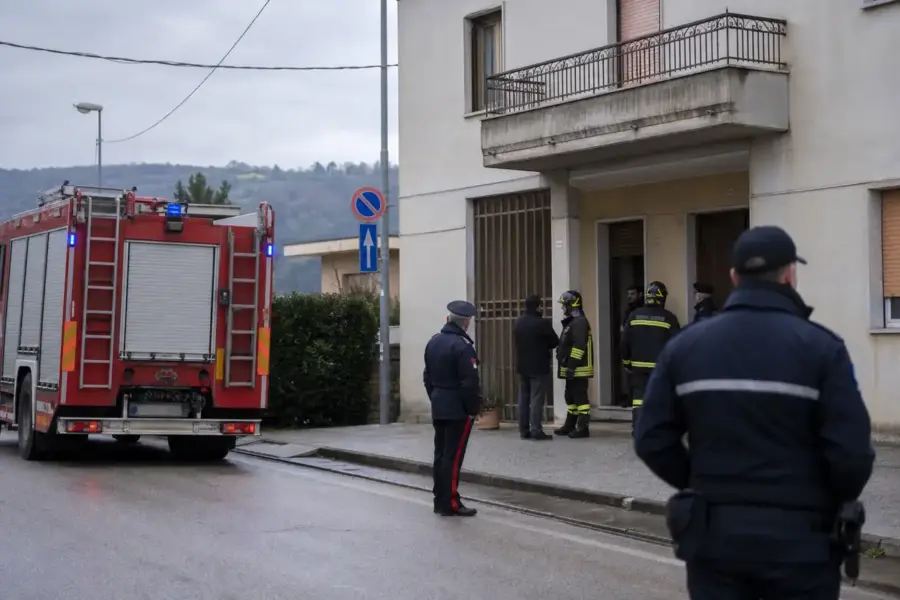 Camion dei vigili del fuoco e carabinieri davanti all’ingresso di un palazzo residenziale in una giornata nuvolosa