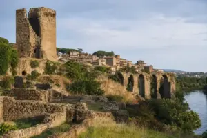 Ruderi in pietra con torre, archi di un antico acquedotto e fiume accanto a un borgo su una collina