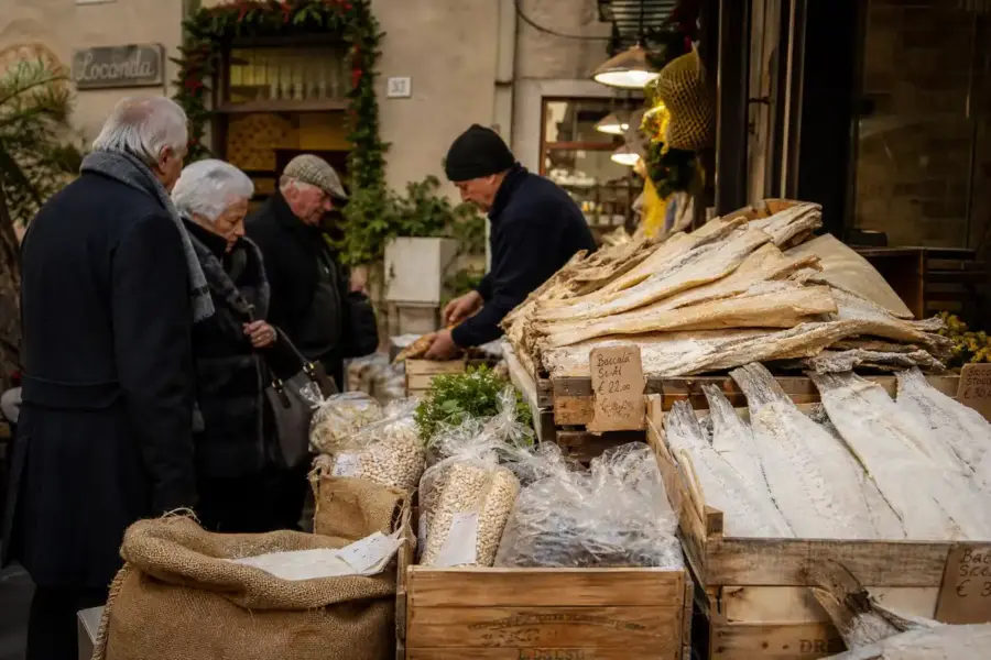 Banco al mercato con filetti di baccalà salato in cassette di legno e clienti in abiti invernali