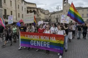 Corteo Pride in una piazza con edifici storici, bandiere arcobaleno e striscione “L’amore non ha genere