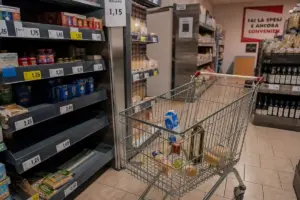 Carrello della spesa quasi vuoto in un piccolo supermercato, tra scaffali con etichette dei prezzi visibili