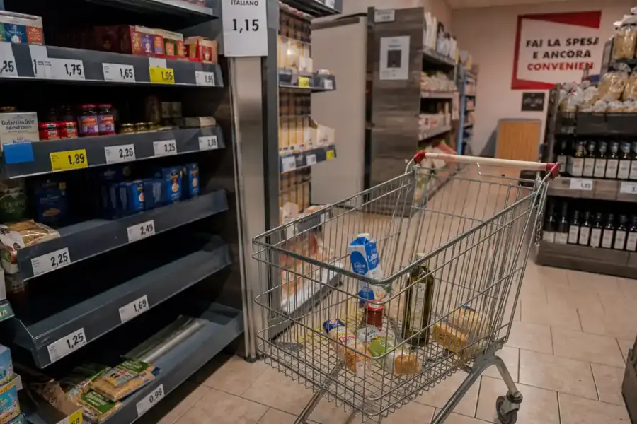 Carrello della spesa quasi vuoto in un piccolo supermercato, tra scaffali con etichette dei prezzi visibili