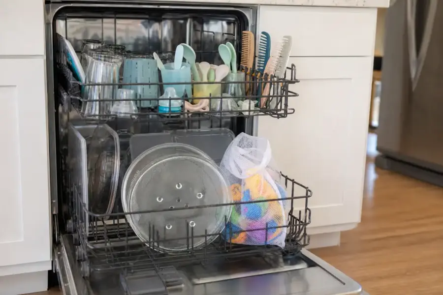 Lavastoviglie aperta con bicchieri, utensili in silicone, pettini, ripiani del frigo e sacchetto a rete con giochi