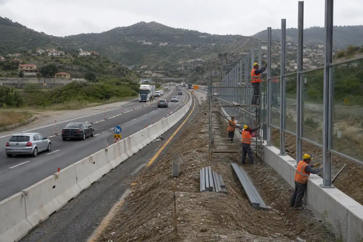 Operai montano barriere antirumore lungo un tratto autostradale con traffico rallentato e deviazione di corsia