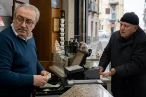 Commerciante alla cassa con banconote in mano mentre un cliente anziano gesticola chiedendo il cambio