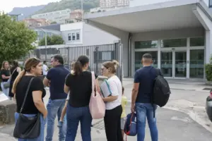 Genitori in attesa davanti all’ingresso di un ospedale, alcuni con documenti in mano e uno zaino da bambino