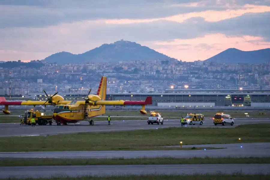 Canadair giallo fermo sulla pista al tramonto con mezzi di servizio e personale aeroportuale