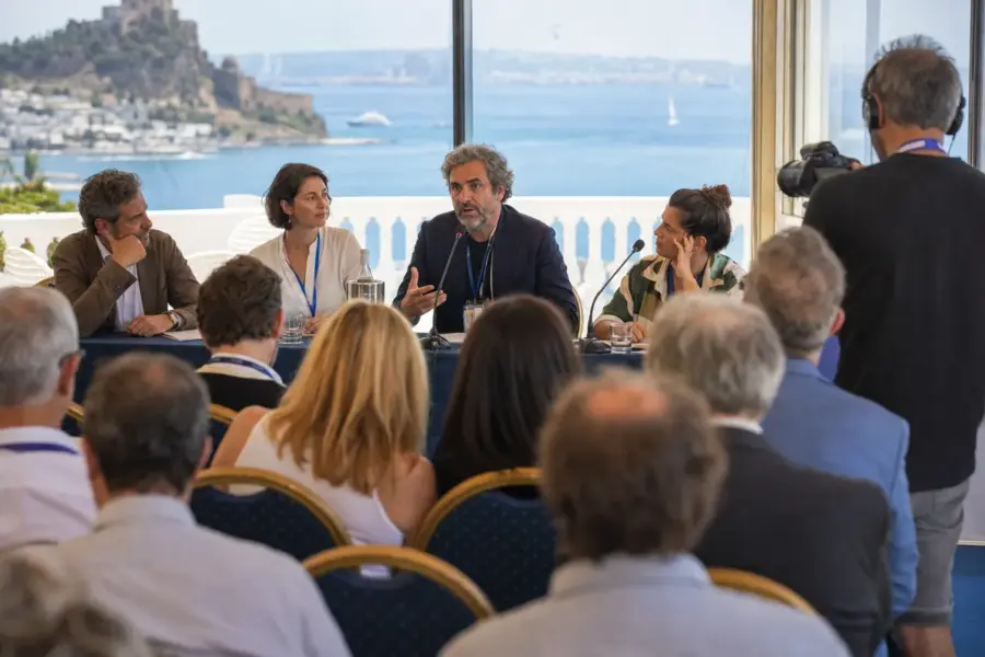 Relatore al microfono in un panel sul cinema con pubblico in sala e vista sul mare da una terrazza
