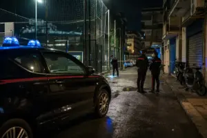 Auto dei carabinieri con luci blu e agenti vicino a un campetto di calcio recintato, in strada di notte