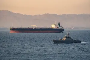 Petroliera in mare con una piccola nave militare di pattuglia in primo piano e costa montuosa nella foschia