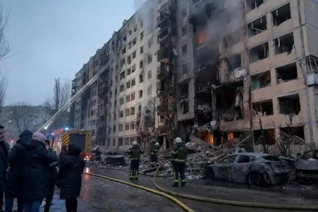 Palazzo residenziale sventrato con fumo e fiamme, vigili del fuoco e auto bruciate in strada