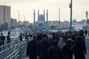 Folla in abiti scuri in fila tra barriere e polizia verso un grande complesso religioso con minareti