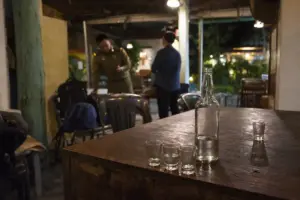 Bottiglia di alcol e bicchierini vuoti su un tavolo in un bar, con due persone sullo sfondo sfocato