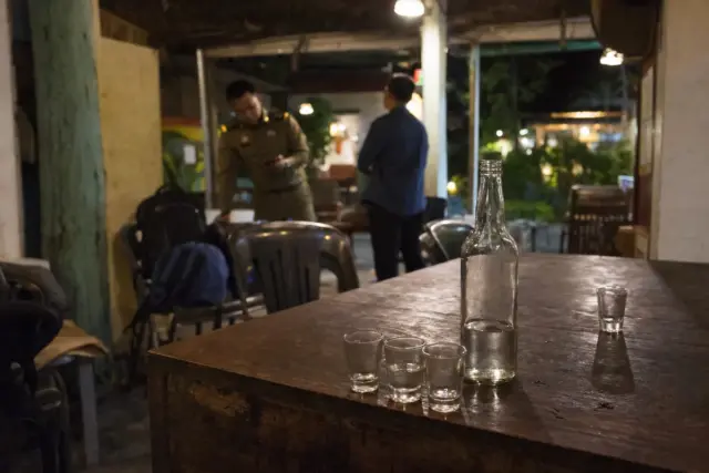 Bottiglia di alcol e bicchierini vuoti su un tavolo in un bar, con due persone sullo sfondo sfocato