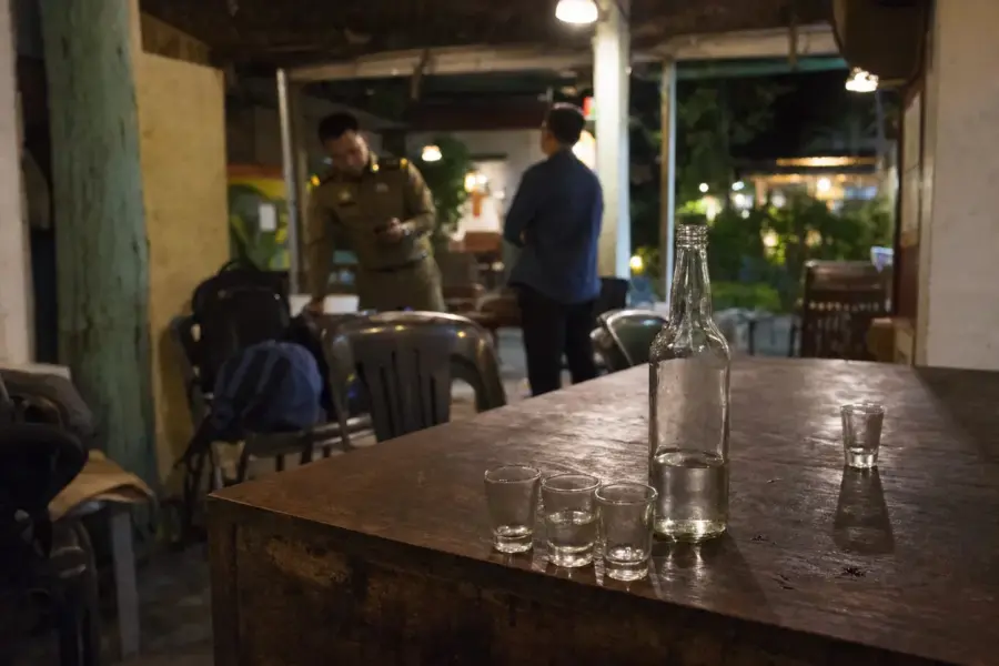 Bottiglia di alcol e bicchierini vuoti su un tavolo in un bar, con due persone sullo sfondo sfocato