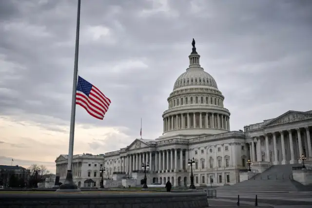 Campidoglio degli Stati Uniti con bandiera americana a mezz’asta sotto cielo nuvoloso