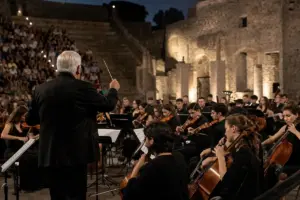 Direttore d’orchestra di spalle con bacchetta davanti a una giovane orchestra in un anfiteatro antico al tramonto