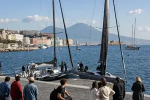 Barche a vela da regata nel porto di Napoli con spettatori sul molo e il Vesuvio sullo sfondo