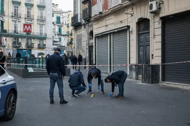Agenti di polizia al lavoro in una piazza, area transennata con nastro e marker delle prove vicino a un ingresso metro
