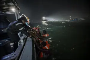 Soccorritori tirano a bordo naufraghi con giubbotti arancioni durante un salvataggio notturno in mare