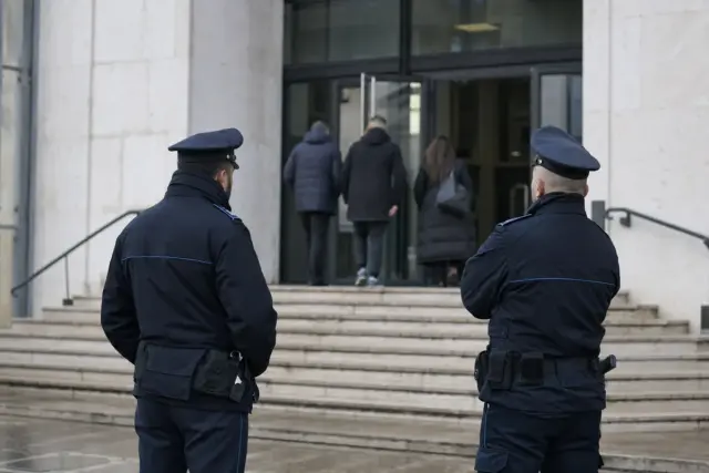 Due agenti di polizia penitenziaria di spalle davanti all’ingresso di un tribunale, con persone che entrano