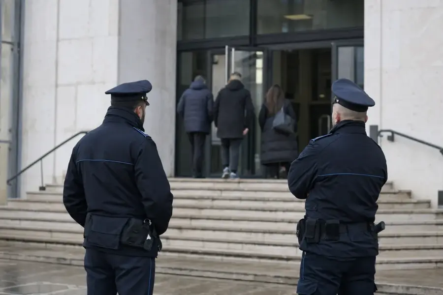 Due agenti di polizia penitenziaria di spalle davanti all’ingresso di un tribunale, con persone che entrano